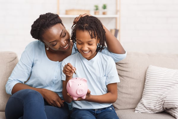 little girl putting money in piggy bank