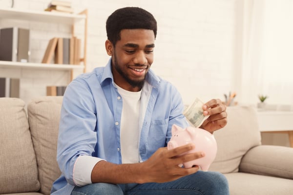 man putting dollar-banknote into piggy bank